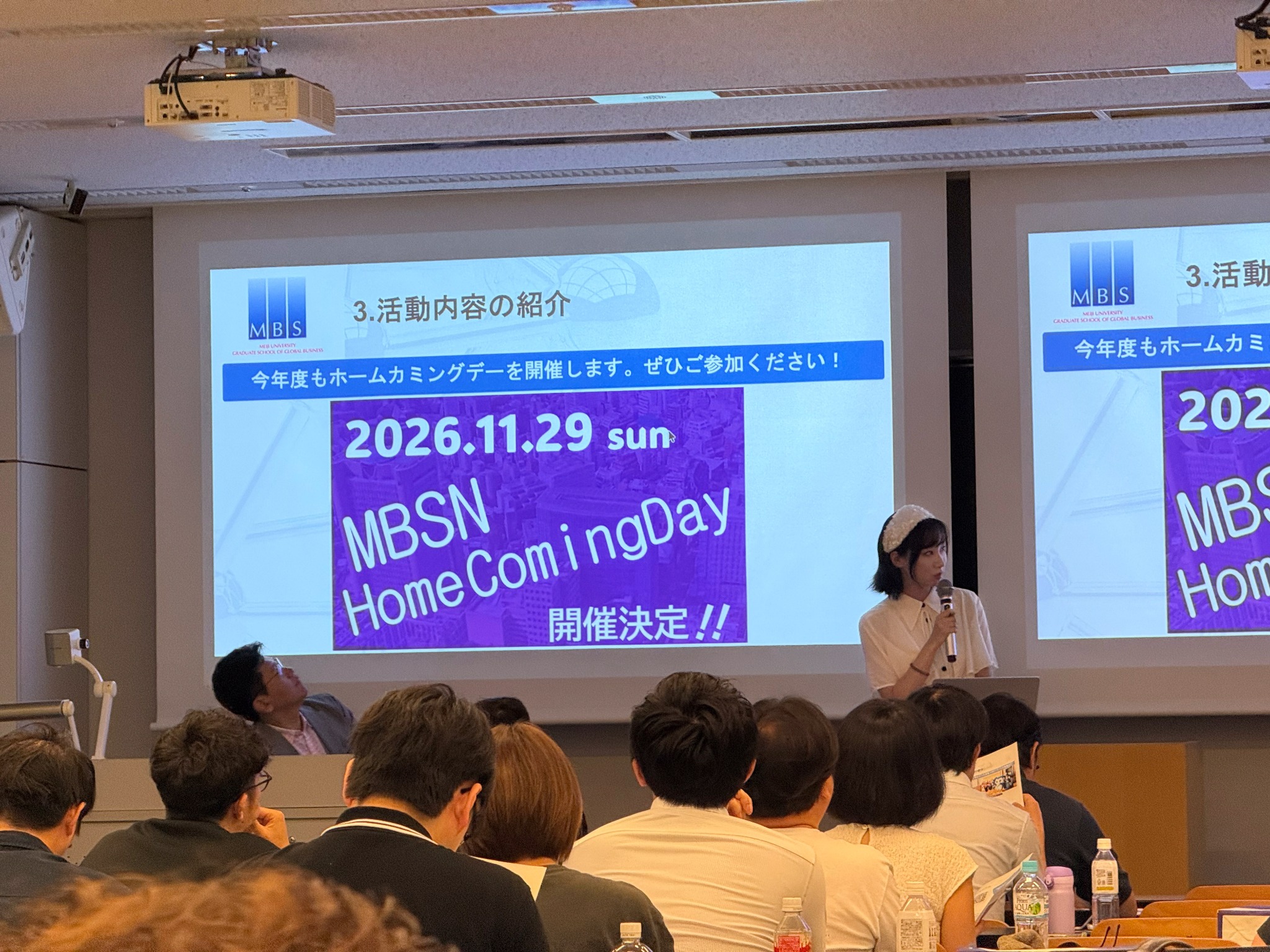 9月20日,星野桜在新生说明会上介绍 MBSN,身后投影展示校友活动信息。
